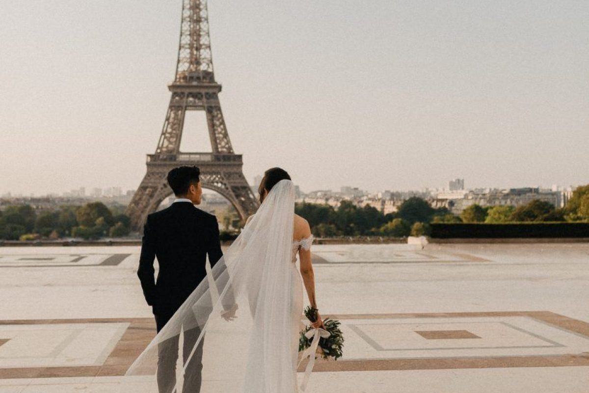 Casal de noivos de costas caminhando diante da Torre Eiffel, em Paris