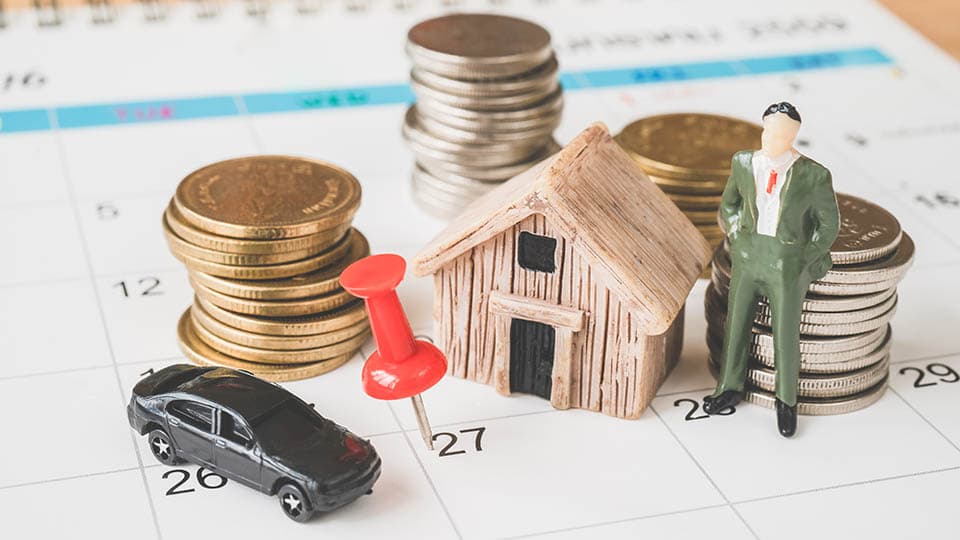 Miniaturas de casa, carro e pilhas de moedas sobre um calendário, representando os bens que podem integrar uma holding