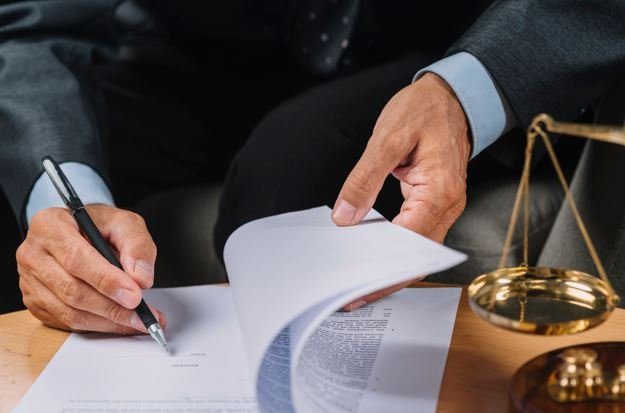 Advogado folheando documentos sobre a mesa, com uma balança da justiça ao lado