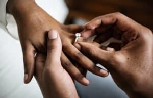 Close das mãos de um casal no momento em que um coloca a aliança de noivado no dedo do outro