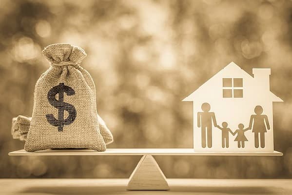 Balança de madeira equilibrando um saco de dinheiro e o recorte de uma casa com uma família