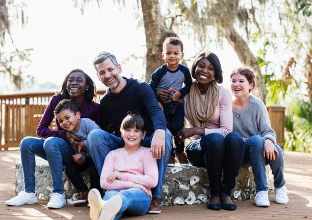 Família reunida ao ar livre, com adultos e quatro crianças sentados lado a lado